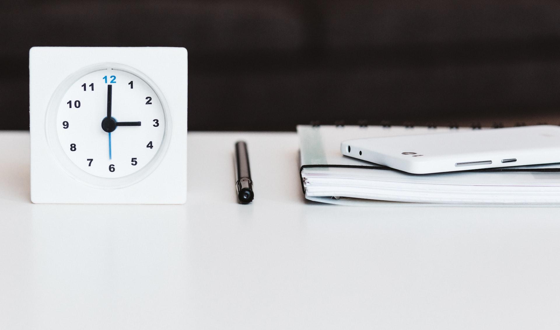 white desk clock near pen and book